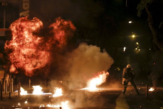 A petrol bomb explodes next to a riot police officer during clashes with hooded youth in Athens