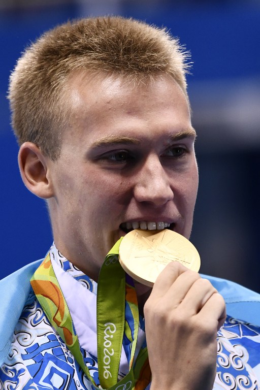 Kazakhstan's Dmitriy Balandin bites his gold medal on the podium after he won in the Men's 200m Breaststroke Final during the swimming event at the Rio 2016 Olympic Games at the Olympic Aquatics Stadium in Rio de Janeiro on August 10, 2016.   / AFP PHOTO / CHRISTOPHE SIMON