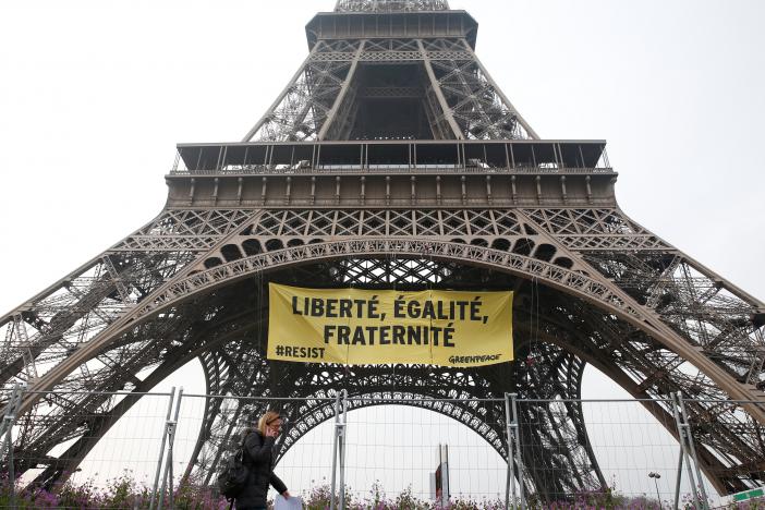 A woman passes by as activists from the environmentalist group Greenpeace unfurl a giant banner on the Eiffel Tower which reads 