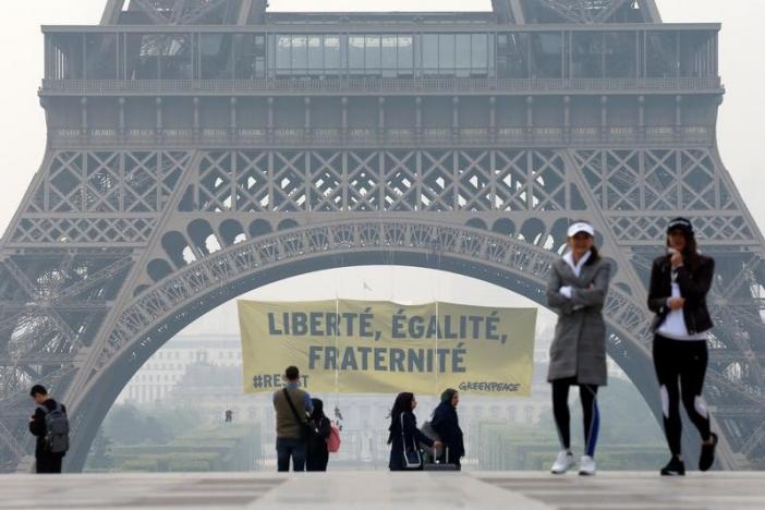 People walk at Trocadero square as activists from the environmentalist group Greenpeace unfurl a giant banner on the Eiffel Tower which reads 